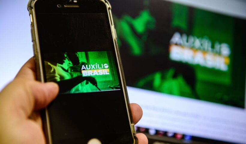 Mão segurando celular conectado ao aplicativo do Auxílio Brasil