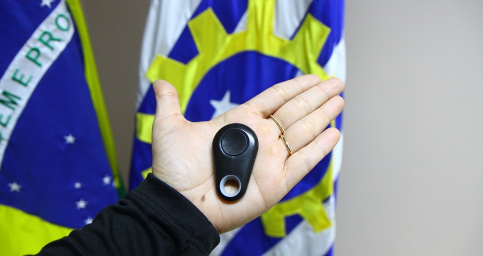 Mão de agente segurando o Botão do Pânico