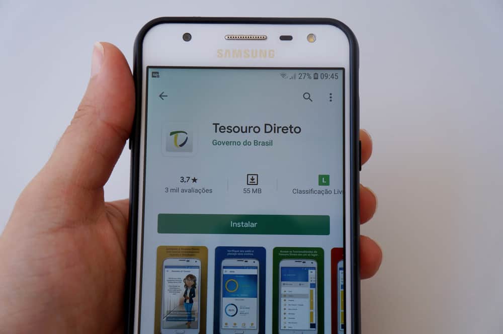 Mão segura celular que mostra Aplicativo do Tesouro Direto
