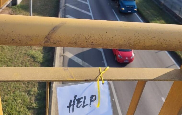 Placa escrito Help (Socorro, em português) presa em passarela na Via Dutra, em ação voltada à saúde mental de pedestres
