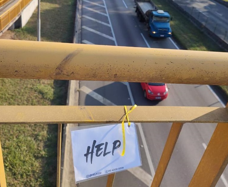 Placa escrito Help (Socorro, em português) presa em passarela na Via Dutra, em ação voltada à saúde mental de pedestres