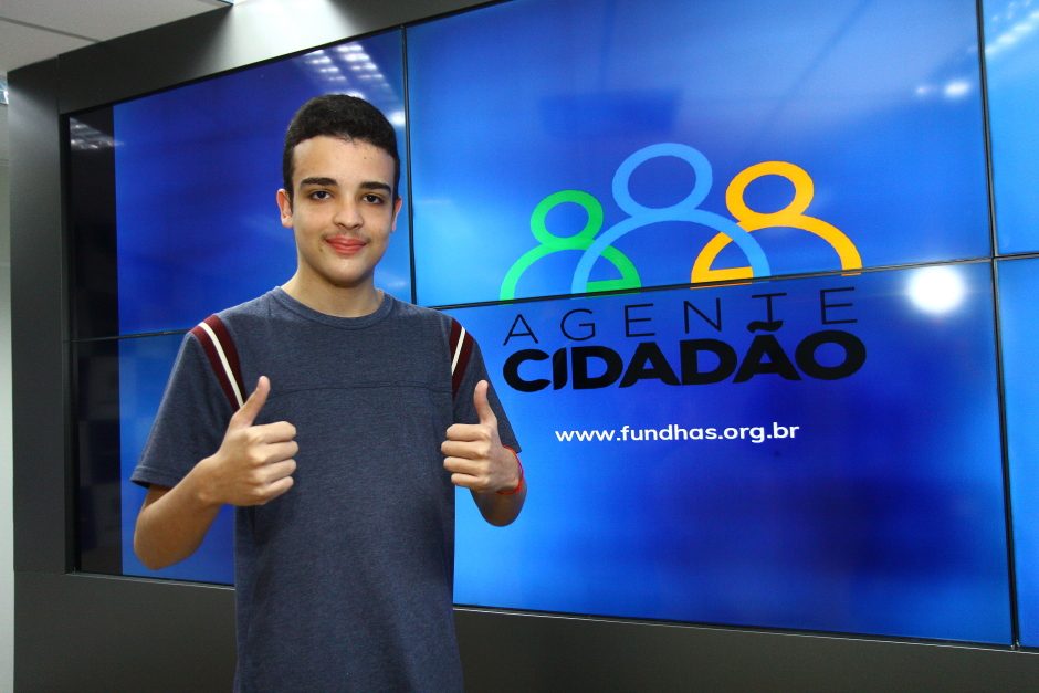 Jovem ao lado do painel do Programa Agente Cidadão