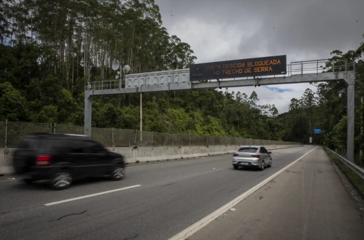 trecho da serra antiga da tamoios, com placa eletronica de avisos e ceu nublado.