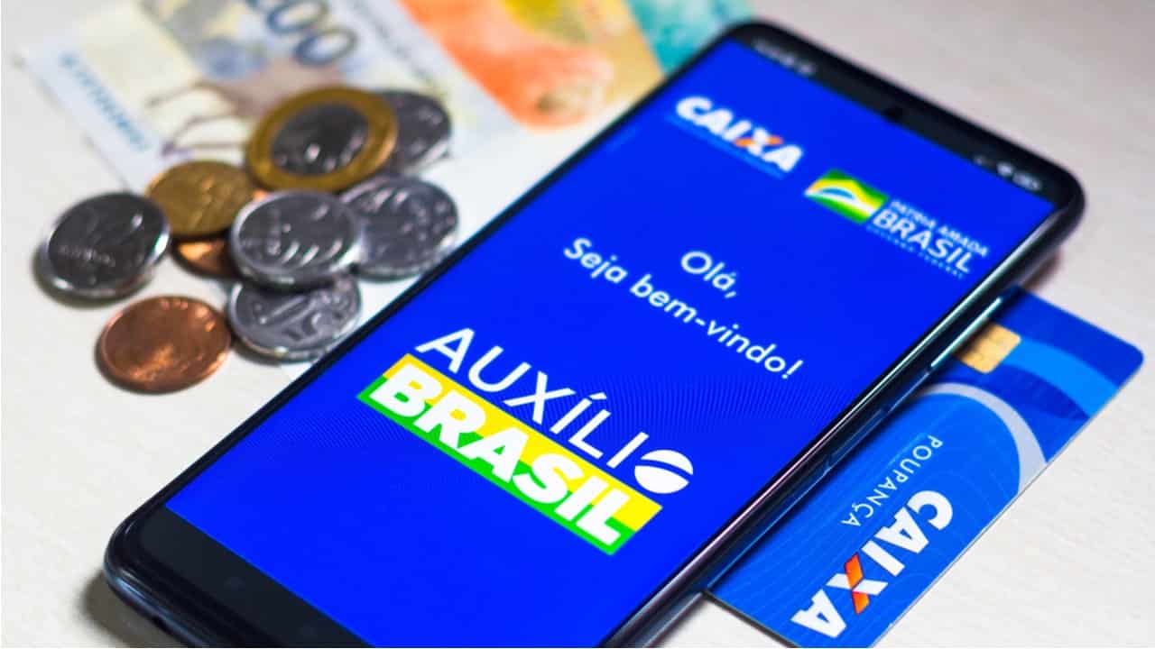 Notas de dinheiro ao lado de celular com app do auxílio Brasil para ilustrar que hoje é pago a última rodada da primeira parcela de 600 reais