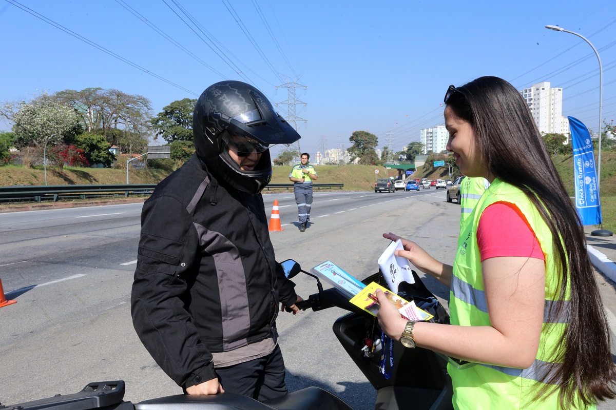 Motociclista sendo orientado por colaboradora da CCR RioSP que ofecere check-up aos profissionais que trabalham com moto
