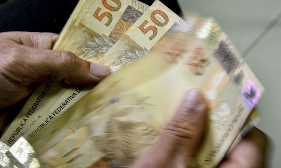 Mãos contando dinheiro. Lula assina hoje (2) MP com novas regras do programa Bolsa Família