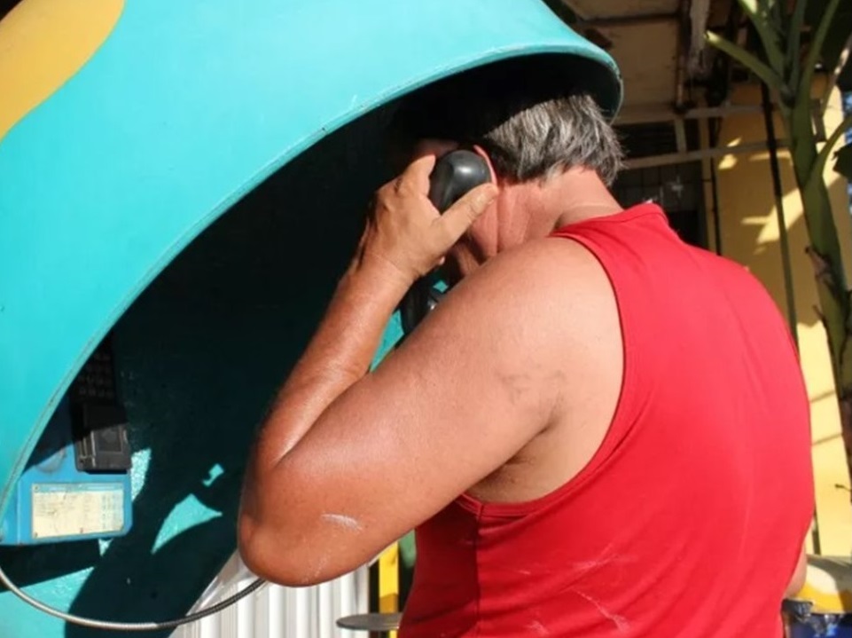 Foto de homem falando em telefone público para ilustrar que Governo de SP irá multar quem passar trote para PM e Bombeiros