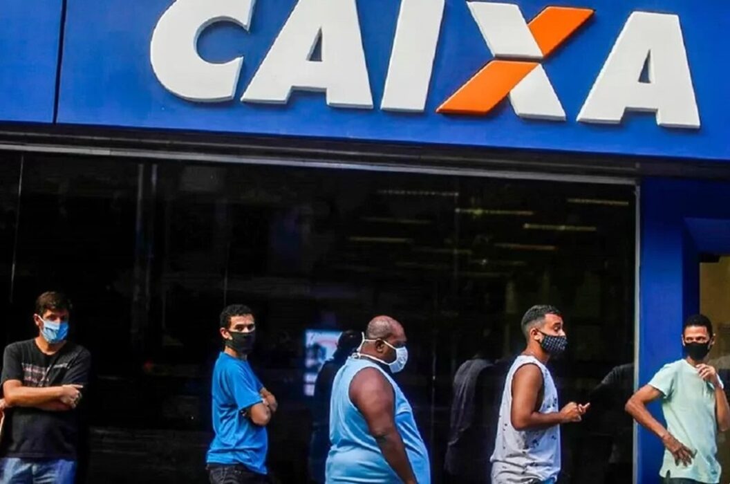 Pessoas com máscaras faciais na fila para entrar em agência da Caixa. Caixa começa a pagar hoje parcela de setembro do Auxílio Brasil