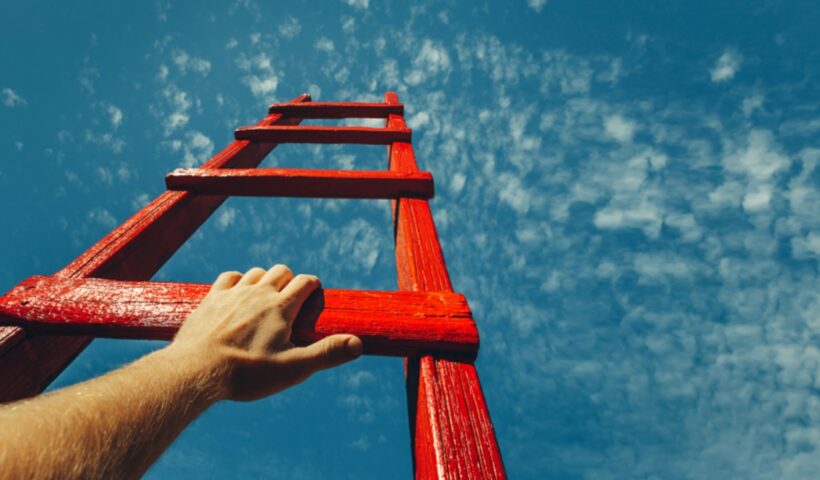 Mão segurando uma escada com o céu azul acima. Imagem ilustra o tema do CBN Mercado de Trabalho, que falou sobre o trabalho com propósito