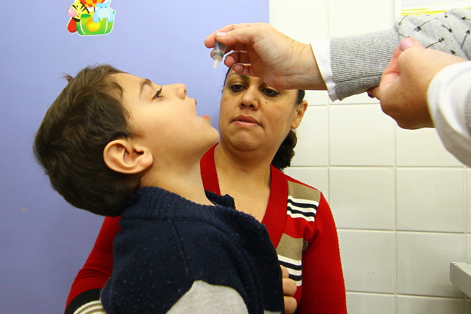 Criança no colo da mãe recebendo a gotinha contra a polio. Parques e shoppings terão vacinação contra a Poliomielite