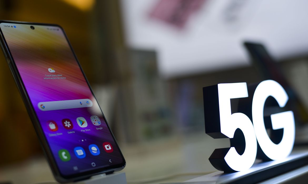 Celular ao lado de luminária com a marca 5G. Anatel libera nesta segunda sinal 5G em mais sete capitais