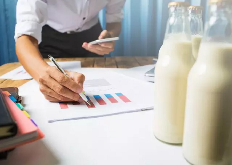 Garrafa de leite ao lado de pessoa analisando gráficos de vendas. Alta do leite
