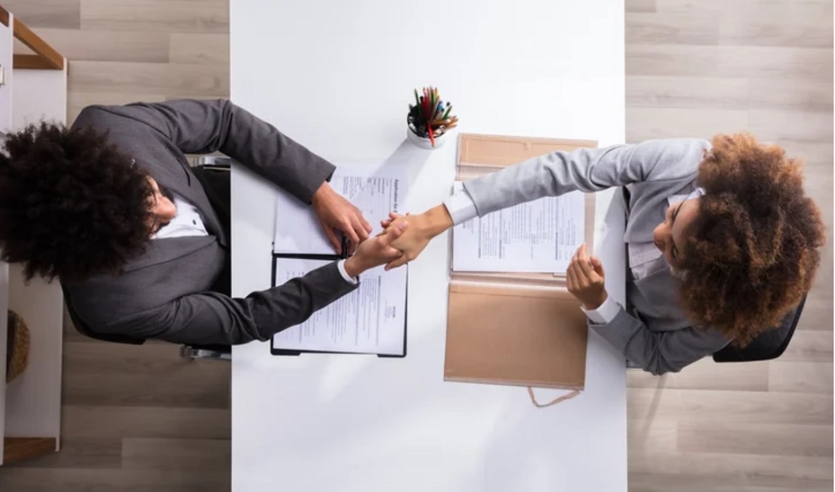imagem vista de cima de duas mulheres apertando as mão em processo seletivo de emprego