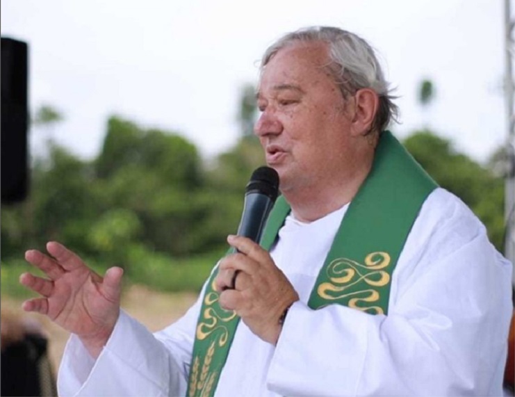 frei hans, que comemora aniversário hoje, fala ao microfone; ele veste traje religioso branco e verde