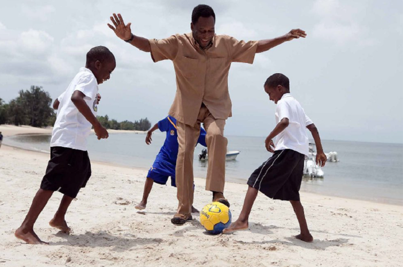 pelé vestido de roupa marrom claro joga bola com três meninos na praia; governos decretaram luto oficial pela morte do rei do futebol