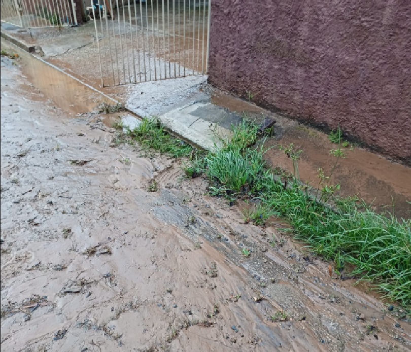 rua cheia de lama, água de chuva ultrapassa limite do portão branco da casa; moradores perdem bens