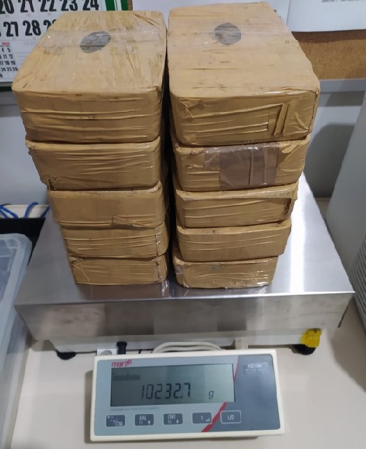 PRF prende passageira com 10kg de cocaína na Dutra; a droga está dividida em 10 tijolos embalados com adesivo marrom; o material está sobre uma balança de pesar