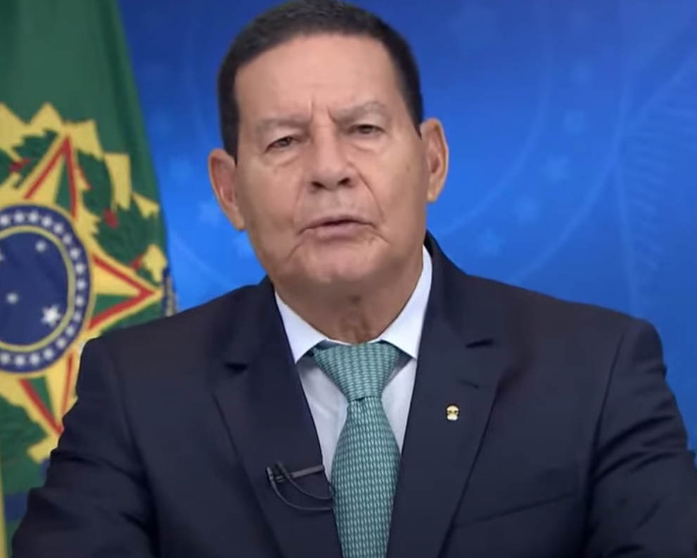 presidente em exercício hamilton mourao faz pronunciamento em rede nacional; ele veste camisa branca, terno azul marinho e gravata azul clara, bandeira do brasil ao fundo