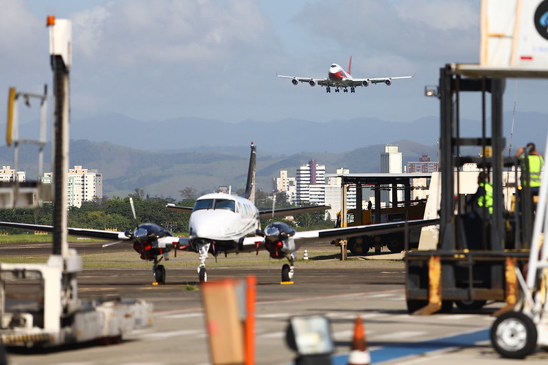 imagem mostra um avião no solo e outro prestes a pousar no aeroporto internacional de sao jose dos campos, que adota tarifas menores para atrair voos