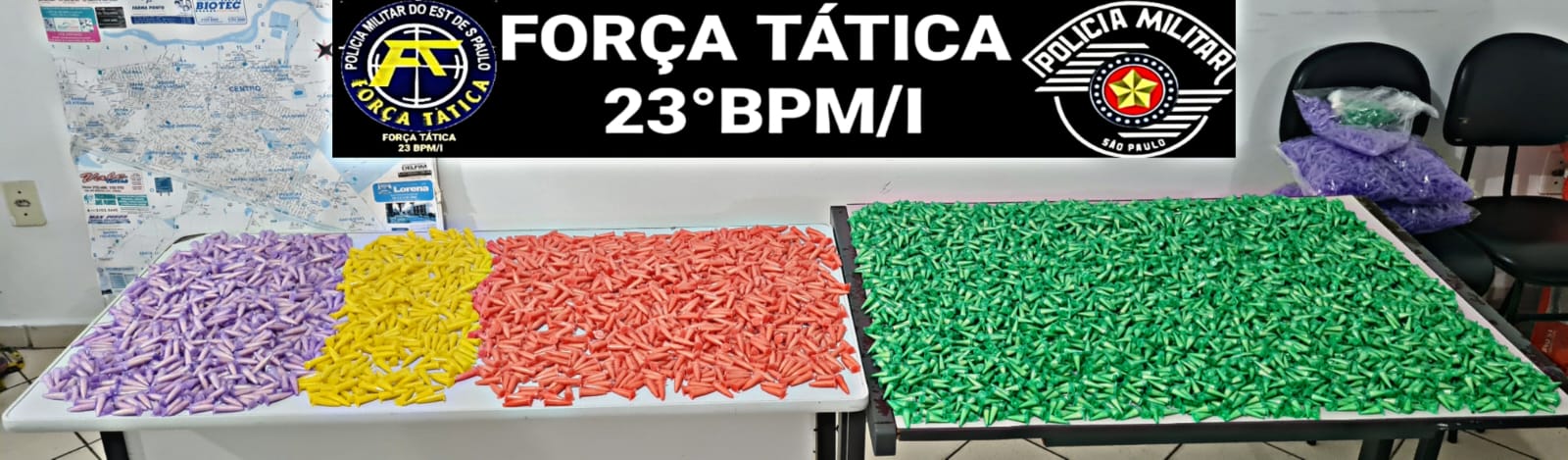 drogas apreendidas sobre mesa da polícia militar; há pinos de cocaína coloridos de amarelo, vermelho e verde; droga armazenada em sacos de ração