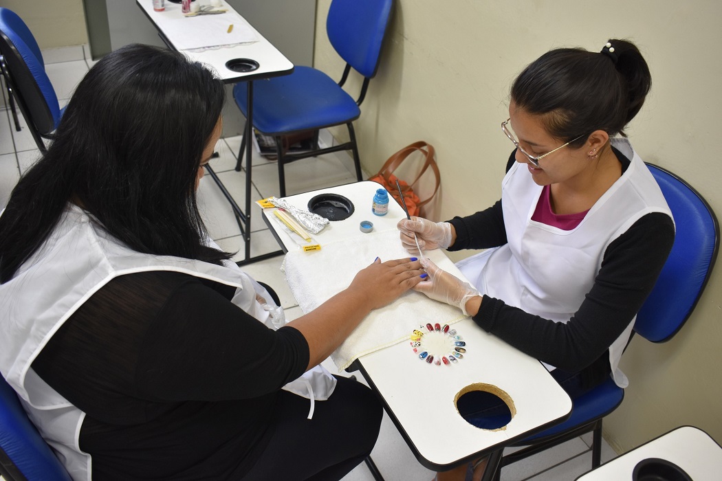 manicure de oculos e avental branco faz as unhas de cliente vestida de preto; escola do trabalho de taubate oferece cursos profissionalizantes gratuitos