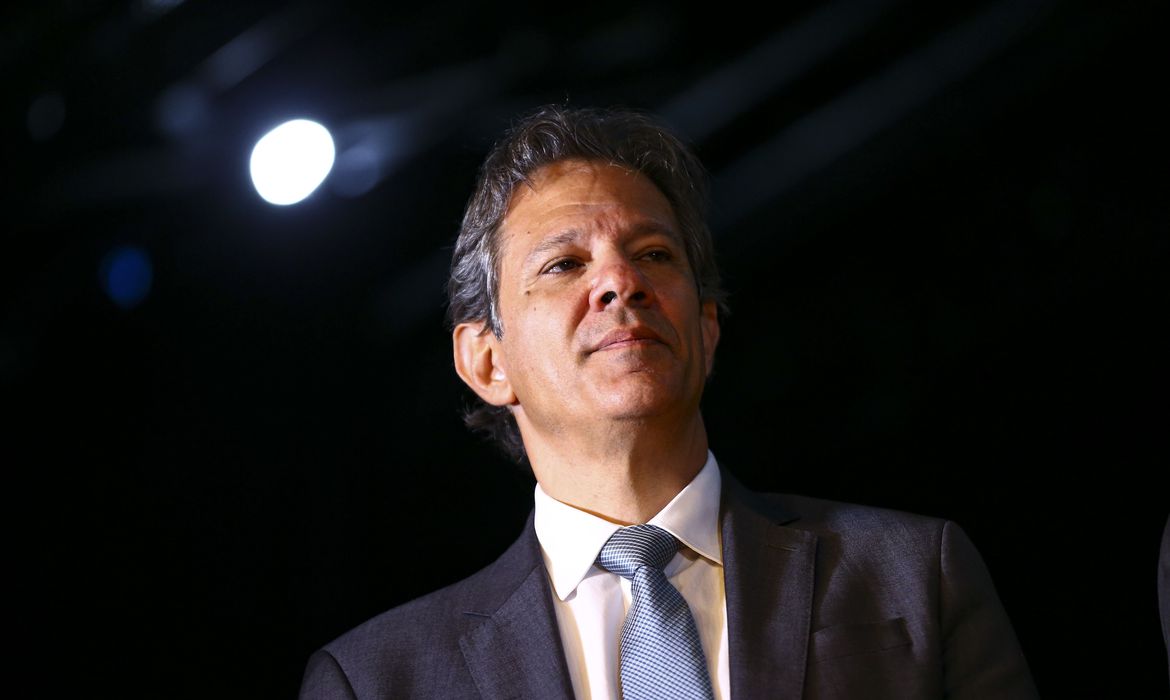 haddad numa sala, com uma lâmpada acesa numa sala escura; ministro diz que salário mínimo reajustado será pago