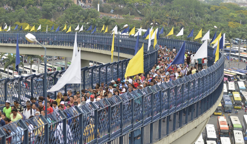 passarela da fé, no santuário nacional de aparecida, liga basílica ao santuário, cheia de fieis; ha bandeiras amarelas e brancas e a via é protegida por grades azuis