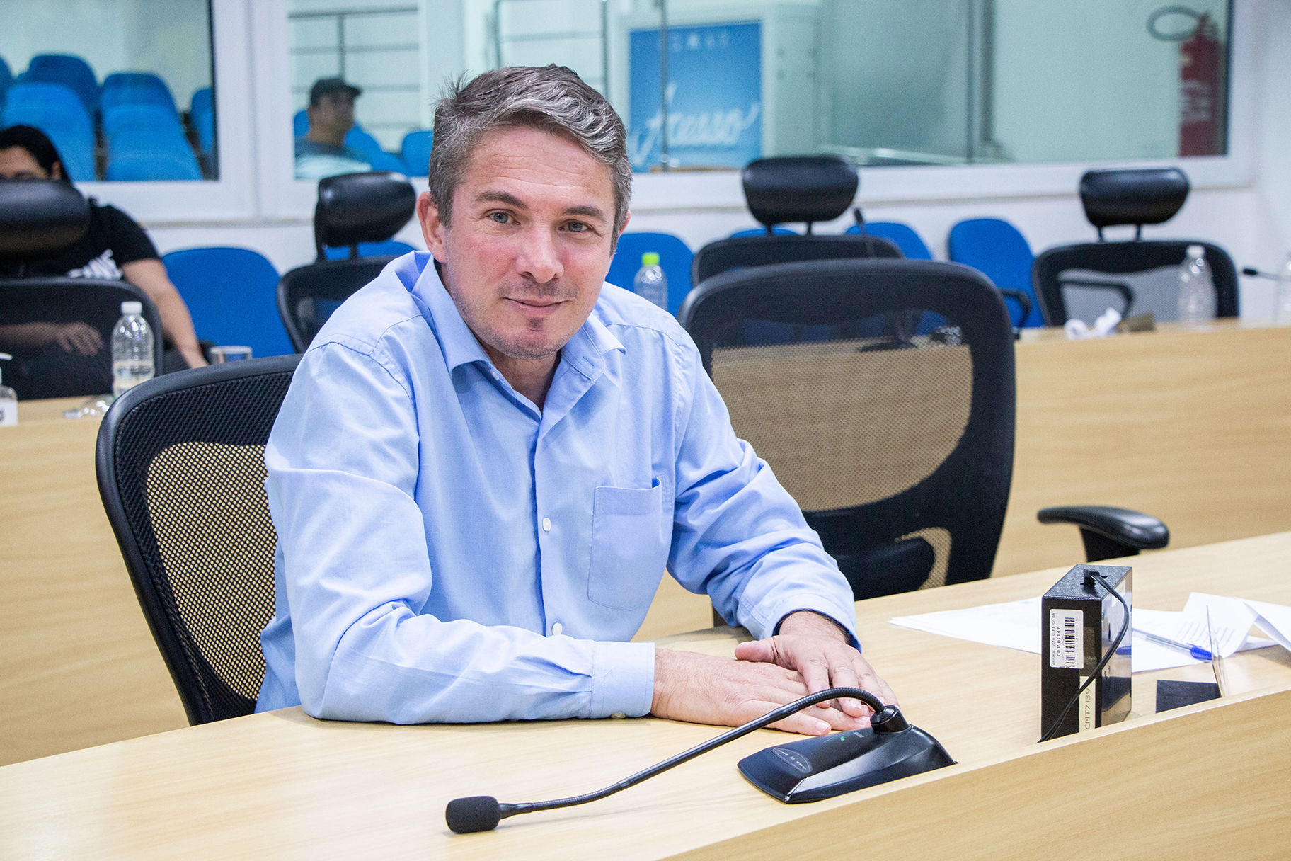 vereador Alberto Barreto, com camisa azul claro, sentado à mesa da camara municipal de taubate, com cadeiras ao fundo, é eleito novo presidente da camara