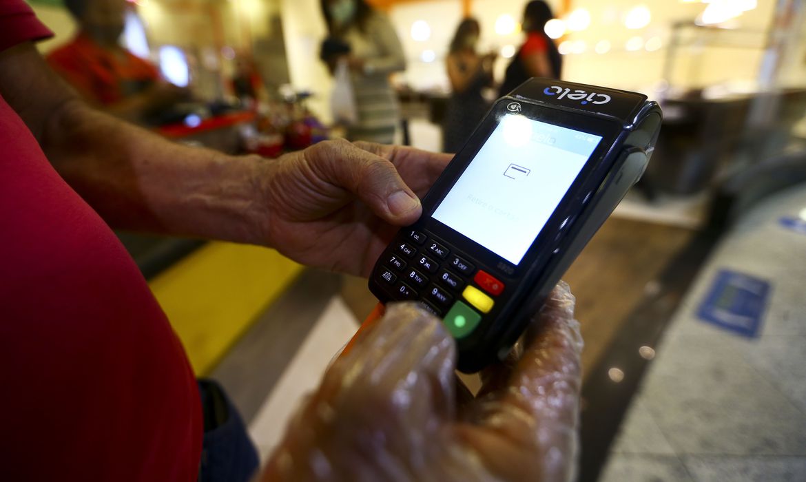 Pessoa segura maquinha de cartão em restaurante. Banco Central deixa de regular cartões de auxílio-alimentação em março