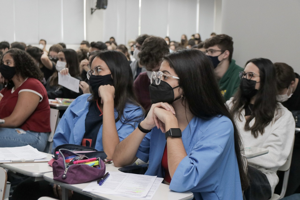 estudantes na sala de aula do poliedro curso, inclusive os do programa de monitoria, com avental azul; todos usam máscara de proteção