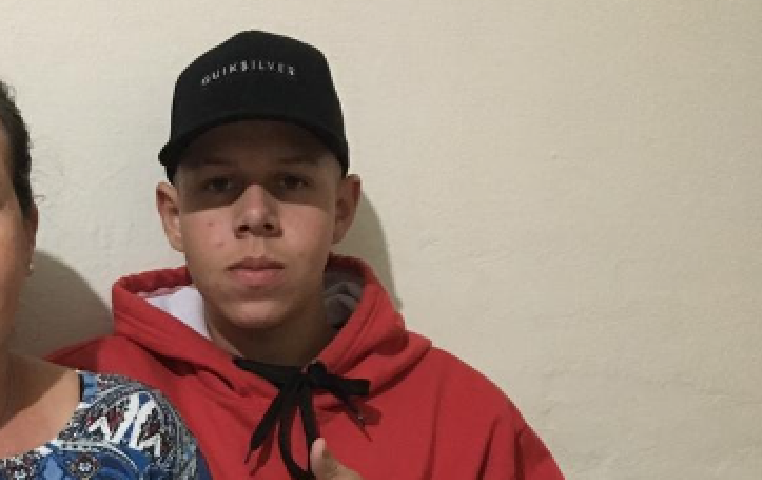 adolescente de 15 anos com boné preto e moletom vermelho faz sinal de positivo com a mao; poiícia investiga assassinato