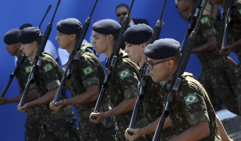 quatro jovens militares com uniforme e boina do exercito seguram armas em desfile; alistamento militar está aberto
