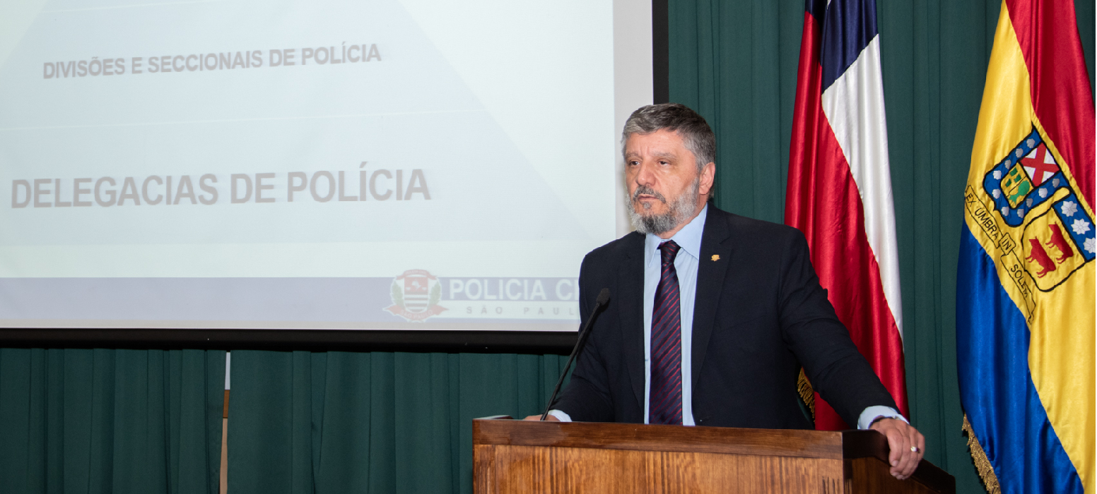 Waldir Antônio Covino Jr., vestido de terno e gravata, fala ao microfone, sobre palco, sobre polícia civil em SP