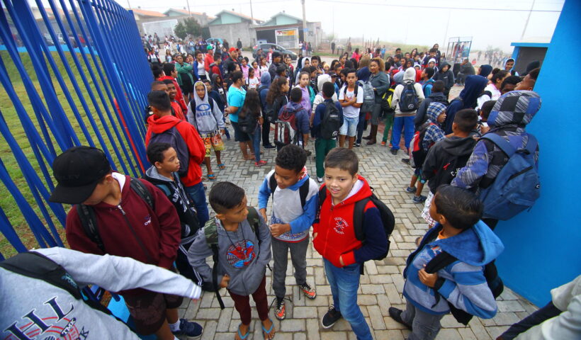dezenas de crianças com mochila entram pelo portão da escola; projeto prevê enfermaria nas escolas