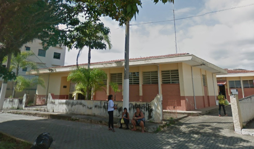 fachada da delegacia de cunha, bege e cor de rosa, com árvore e pessoas sentadas em frente; polícia civil investiga homicídio e suicídio