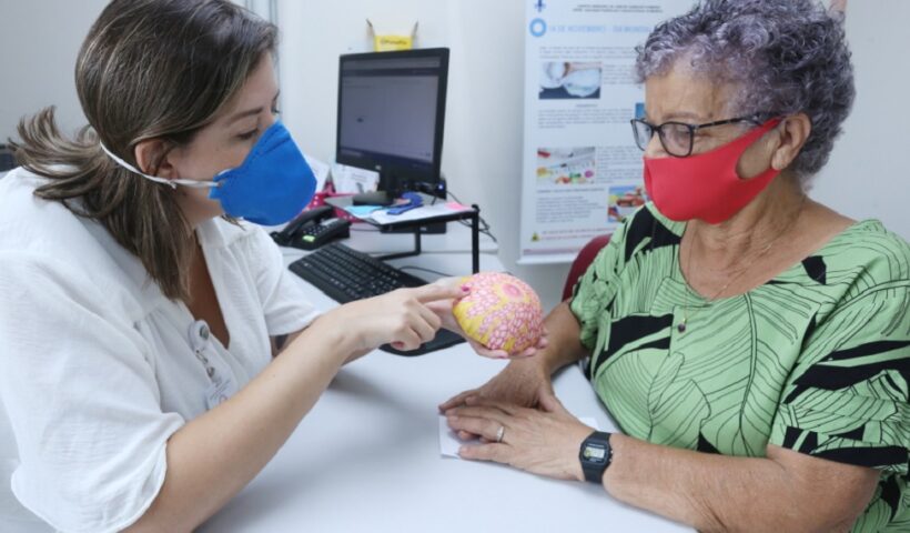 Médica mostrando para paciente, molde de réplica de mama. Prefeitura anuncia aumento de Vagas de mamografia