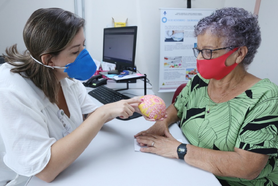 Médica mostrando para paciente, molde de réplica de mama. Prefeitura anuncia aumento de Vagas de mamografia