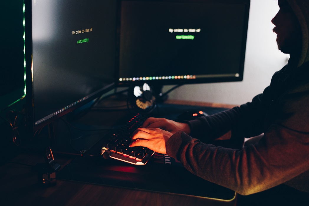 código malicioso: Homem suspeito em computador num ambiente escuro.