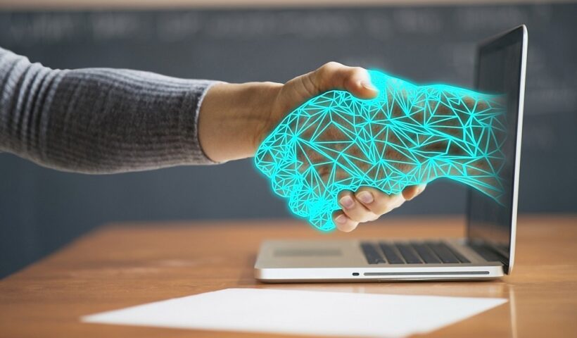 Mão humana apertando mão virtual saindo de tela de computador. CBN Inovação fala sobre profissões do futuro