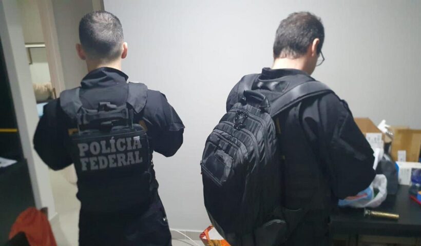 Dois agentes da PF de costas averiguando mídias eletrônicas. Pornografia infantil: PF cumpre mandado de busca e apreensão em São José dos Campos