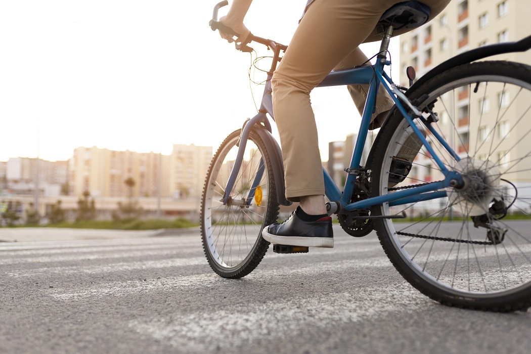 Imagem mostar rodas de bicicleta com destaque para perna de ciclista pedalando em faixa de segurança em rua. Mobilidade Urbana em Taubaté recebe Fórum nesta quinta-feira (24/08)