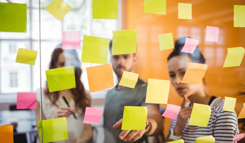 Invovação organizacional: Jorvens executivos olhando para um painel de vidro com diversos post-its grudados