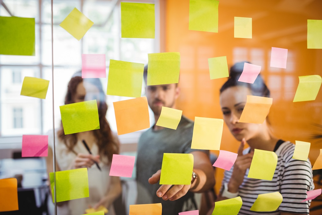 Invovação organizacional: Jorvens executivos olhando para um painel de vidro com diversos post-its grudados