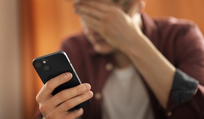 Homem com mão no rosto, preocupado, segurando celular. Portabilidade numérica: Anatel adota novas medidas para evitar fraudes