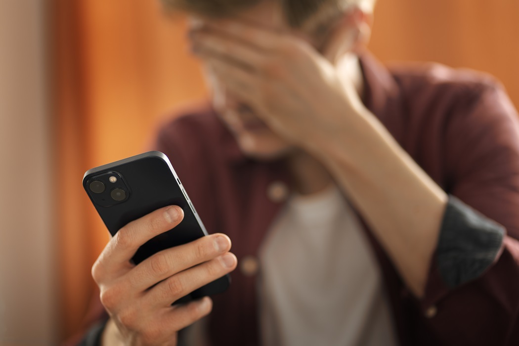 Homem com mão no rosto, preocupado, segurando celular. Portabilidade numérica: Anatel adota novas medidas para evitar fraudes