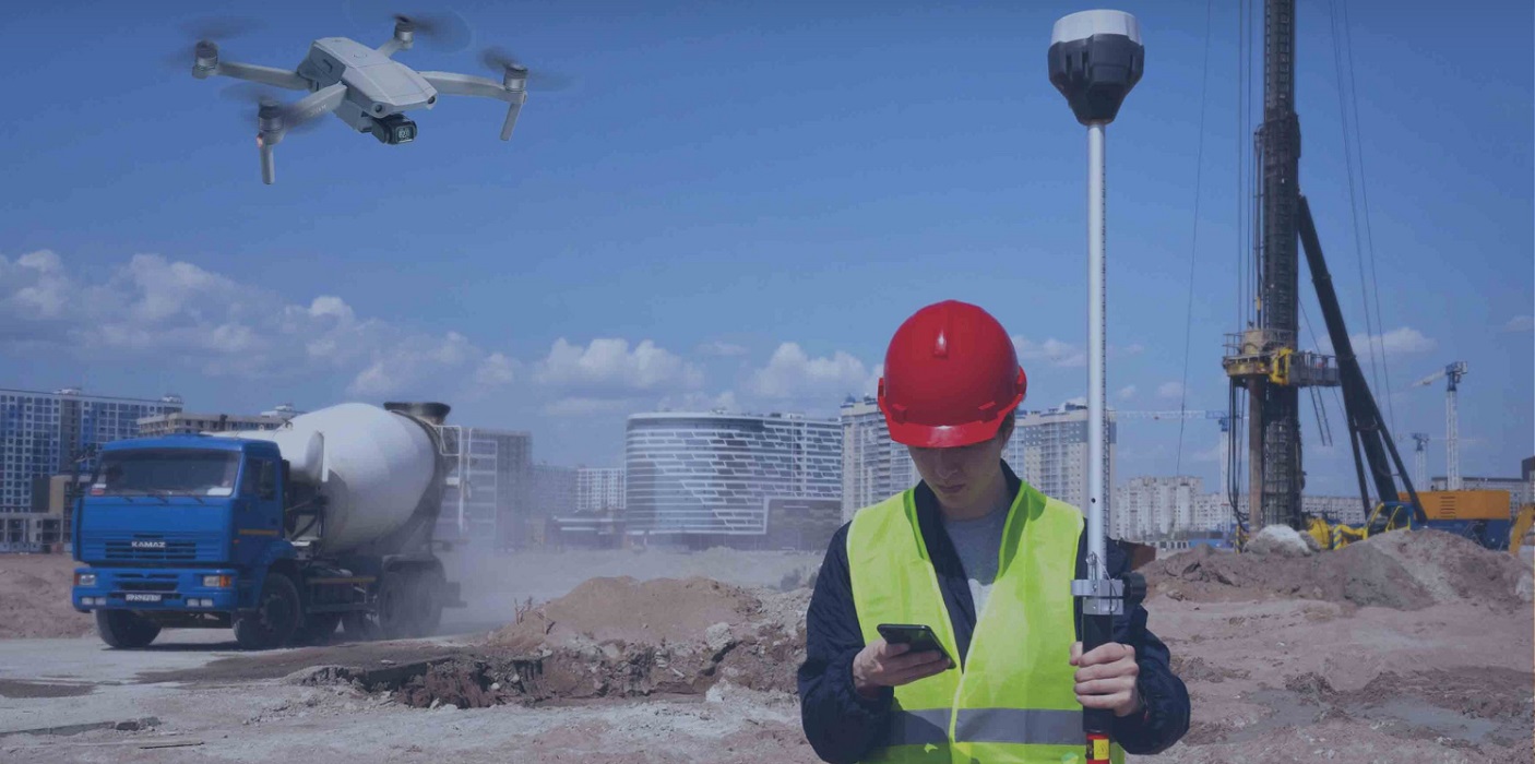 fundionário de contrução civil segurando celular com app para o setor, ao lado de drone e caminhão