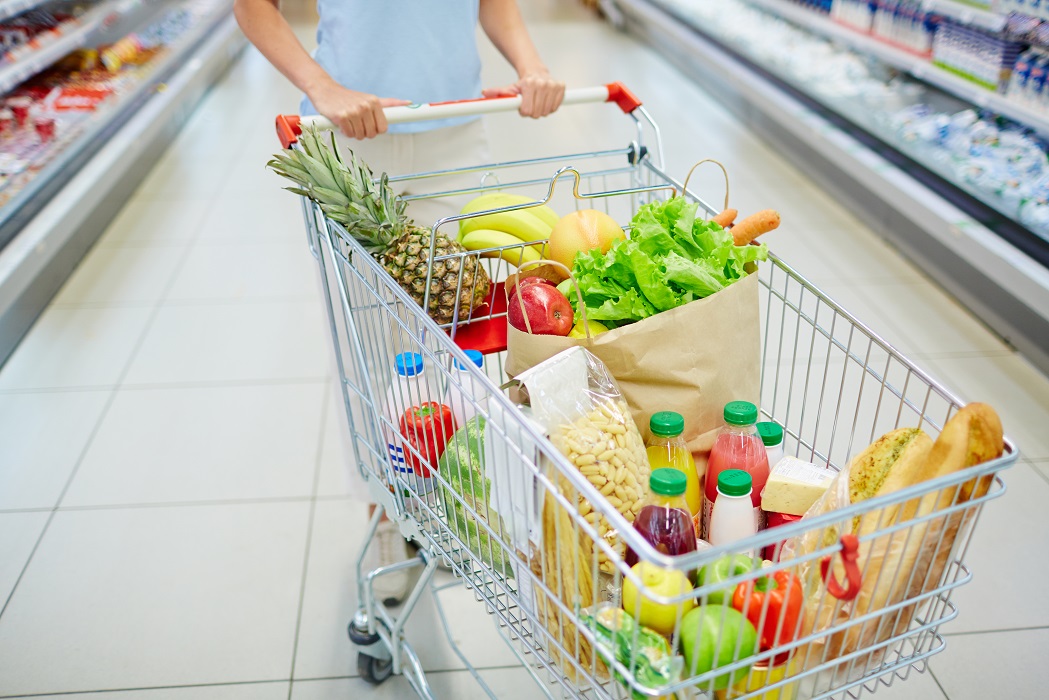 Carrinho de de supermercado com diversos produtos alimentícios sendo empurrados por mulher. Cesta básica tem a quinta redução de preços no Vale do Paraíba, afirma NUPES