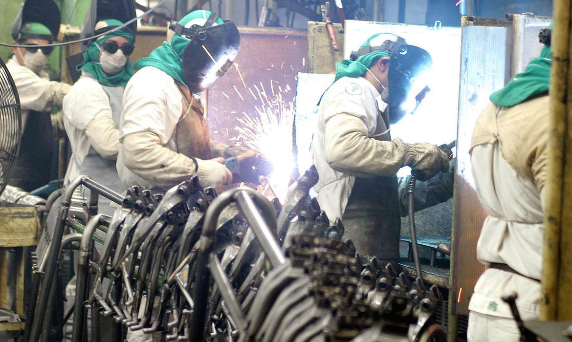 Funcionários de metalúrgica utilizando equipamentos de segurança em processo de soldagem em indústria. Mercado eleva para 2,56% projeção do crescimento da economia em 2023