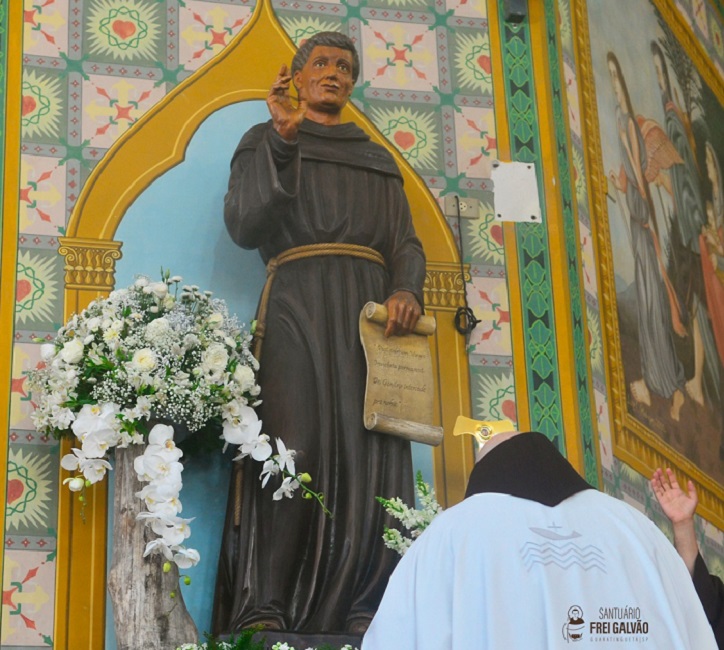 Imagem de frei Galvão, com religioso de costas se curvando frente à imagem.