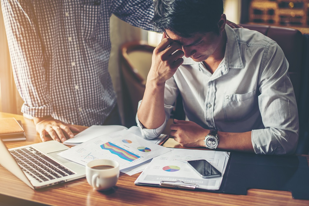 Um jovem empresário sério olhando para o relatório financeiro parece algo errado com seu chefe no cargo. CBN Mercado de Trabalho: Fiquei desempregado. E agora, o que fazer?